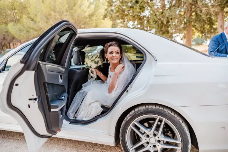 Bride seated in the white wedding car with the door open, bouquet in her lap