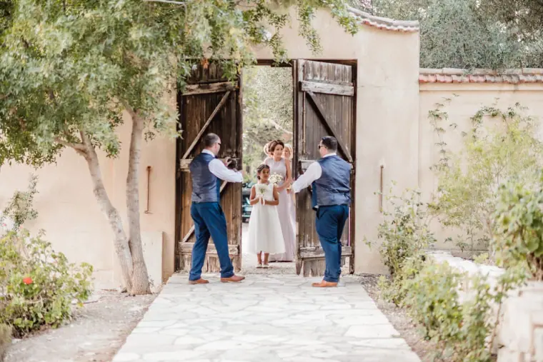 Groomsmen opening the old wooden gates of the monastery courtyard at Minthis Hills