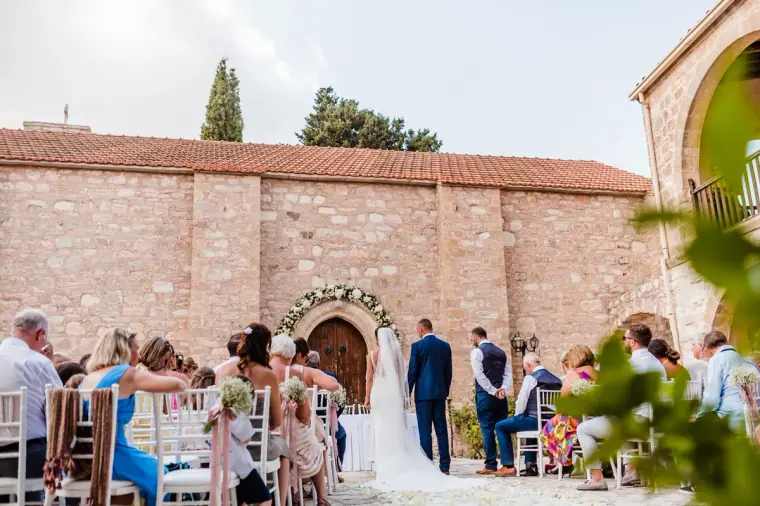 Wide view of the courtyard ceremony beside the old stone monastery chapel at Minthis Hills