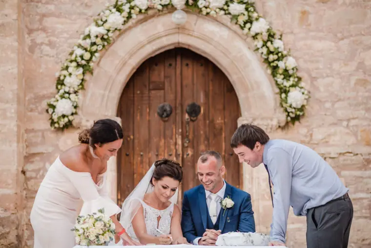 Kaye and Matt signing the register at a table before the chapel's wooden door