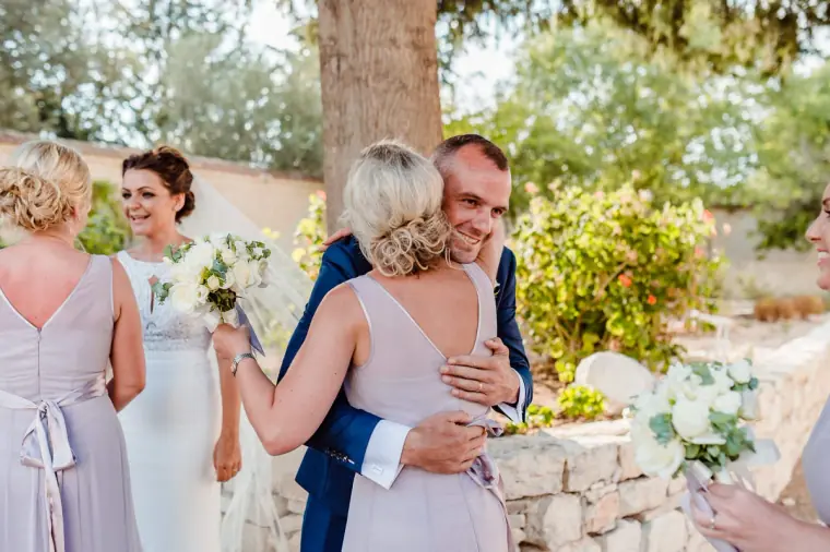 Bridesmaid in lilac hugging the groom as guests offer congratulations