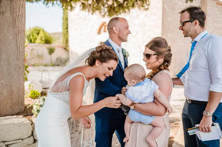 Bride smiling at a baby held by a guest after the ceremony