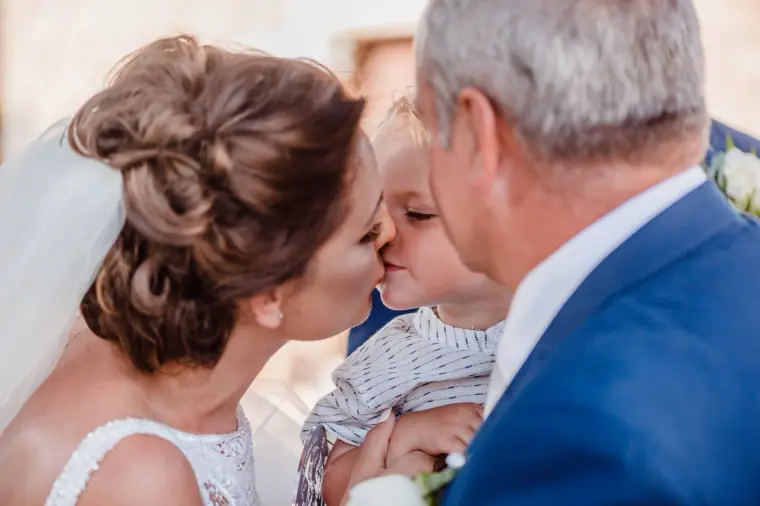 Bride kissing a small child held by an older guest in a navy suit