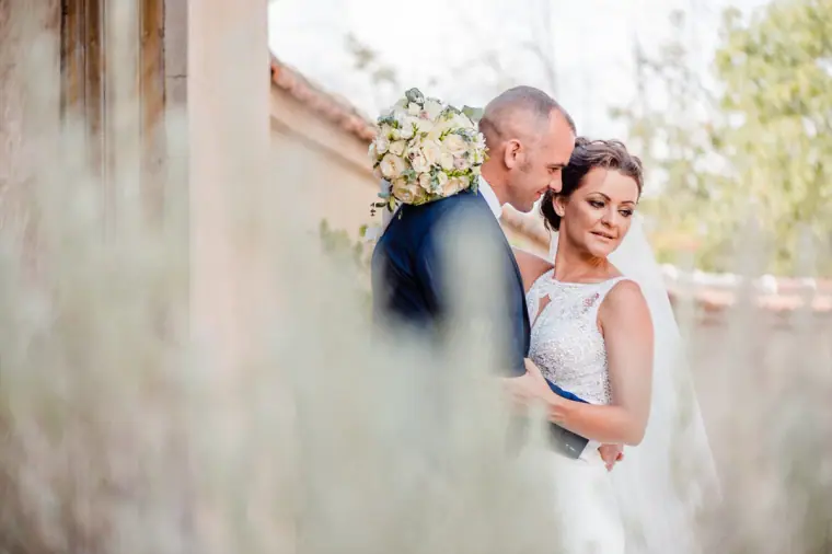 Groom holding the bride close, framed by blurred lavender and stone walls