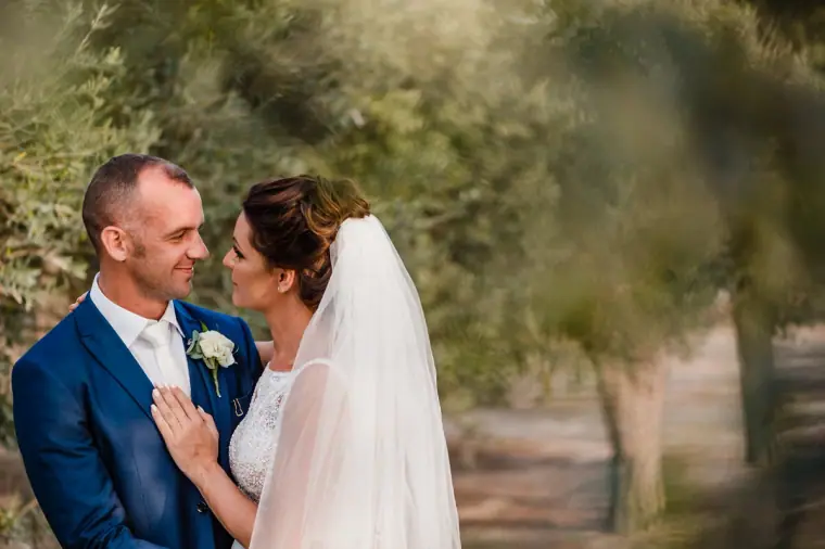 Groom with his hand on the bride's shoulder among olive trees