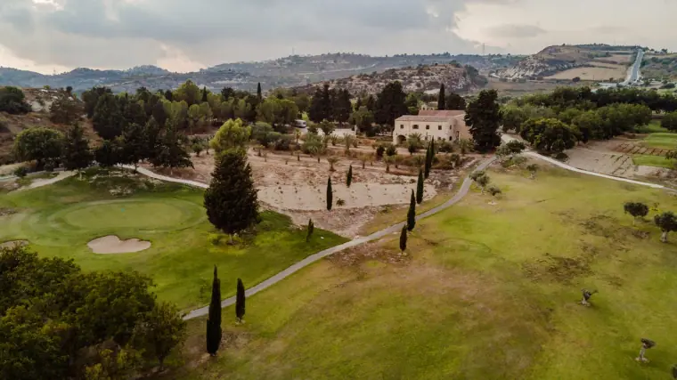 Drone view over green fairways and cypress trees towards the old monastery