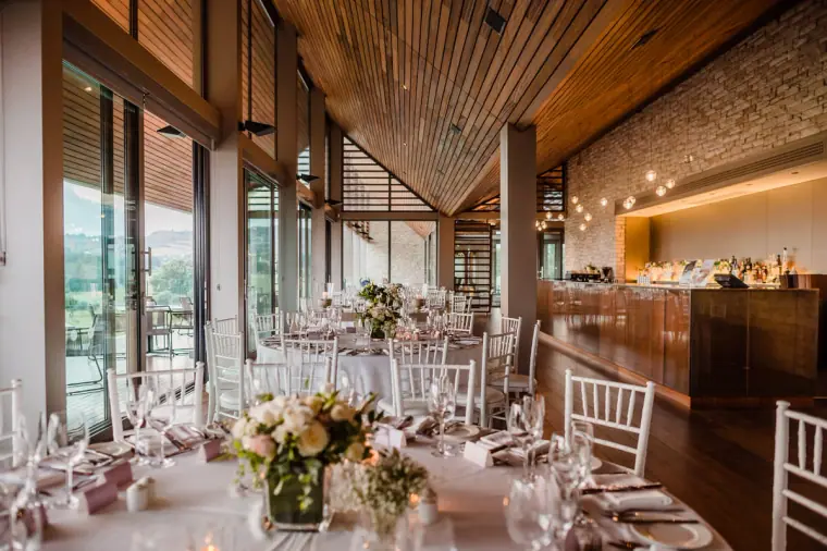 Round tables dressed with white and blush flowers in the timber-ceilinged dining room