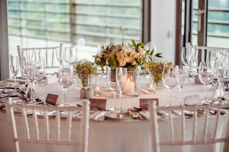 Close-up of a reception table with rose centrepiece, glassware and white Chiavari chairs