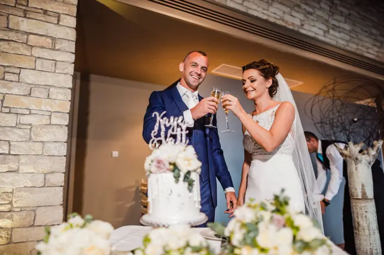 Bride and groom toasting with Champagne beside their wedding cake