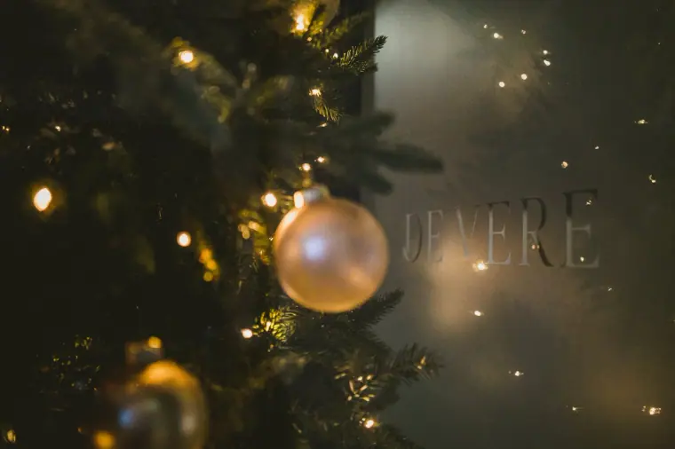 Gold bauble on a Christmas tree with the De Vere sign glowing behind