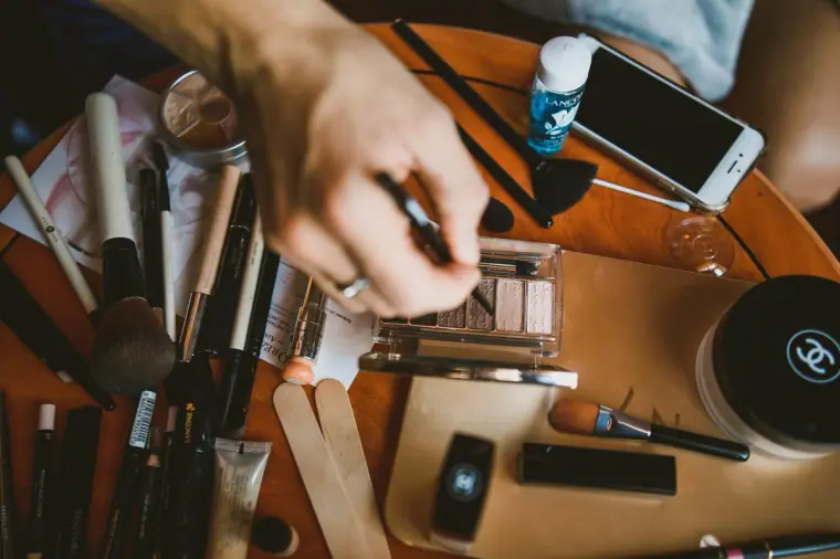 Make-up artist's brushes and palettes spread across a wooden table