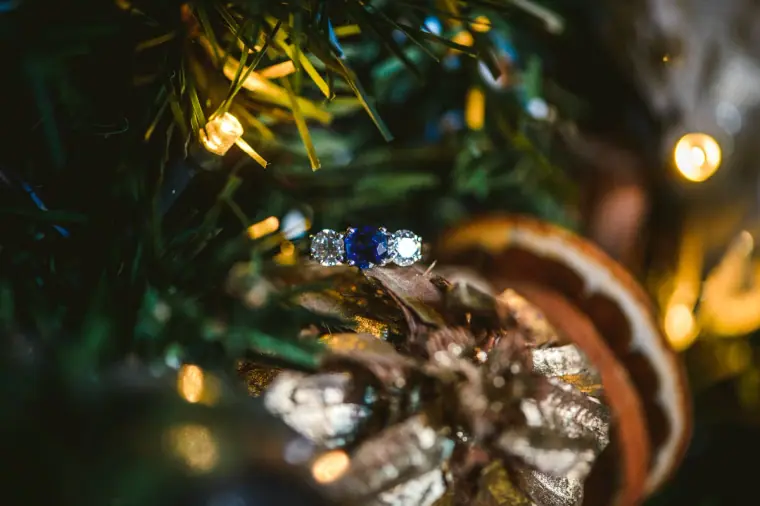 Sapphire engagement ring nestled among Christmas tree lights and a dried orange slice