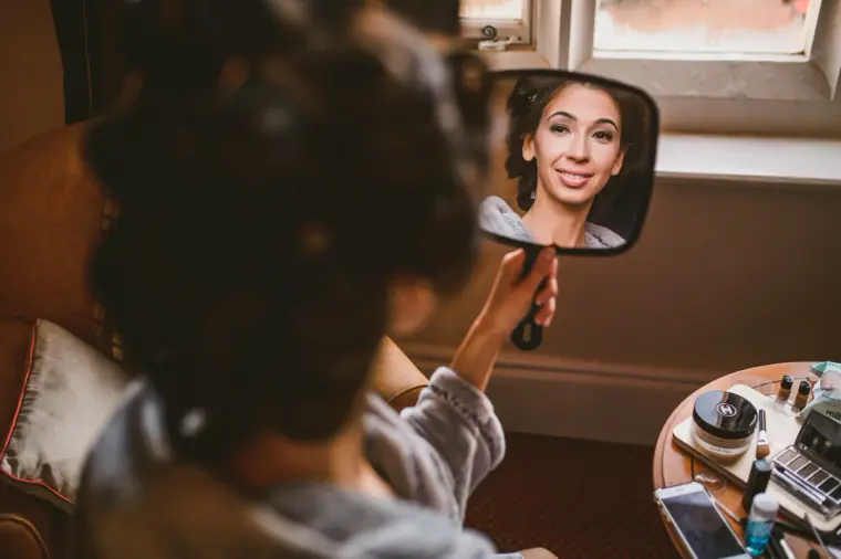 Bride checking her make-up in a hand mirror as she gets ready