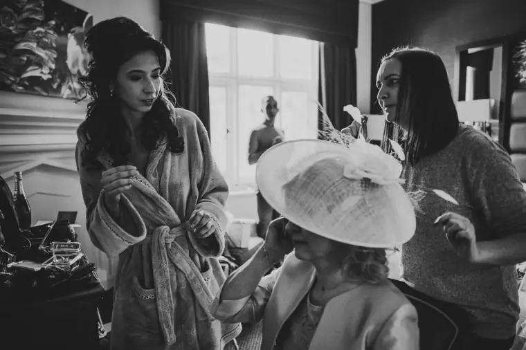 Black-and-white photo of the bridal party getting ready, one holding a wide-brimmed hat
