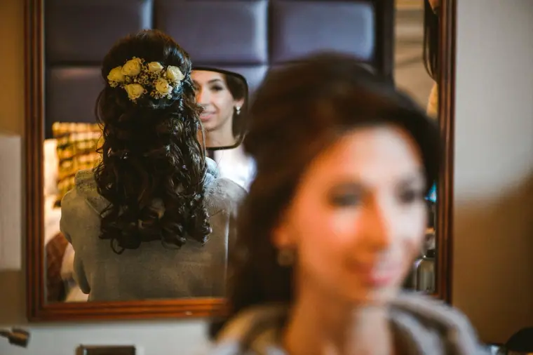 Bride's flower-adorned curls reflected in a mirror as she gets ready