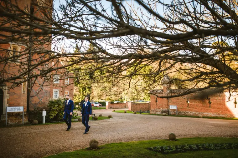 Groom and best man walking across the forecourt of Wotton House under bare branches