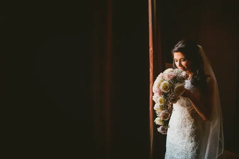 Elina holding her bouquet by a window in her lace gown and veil at Wotton House, Dorking