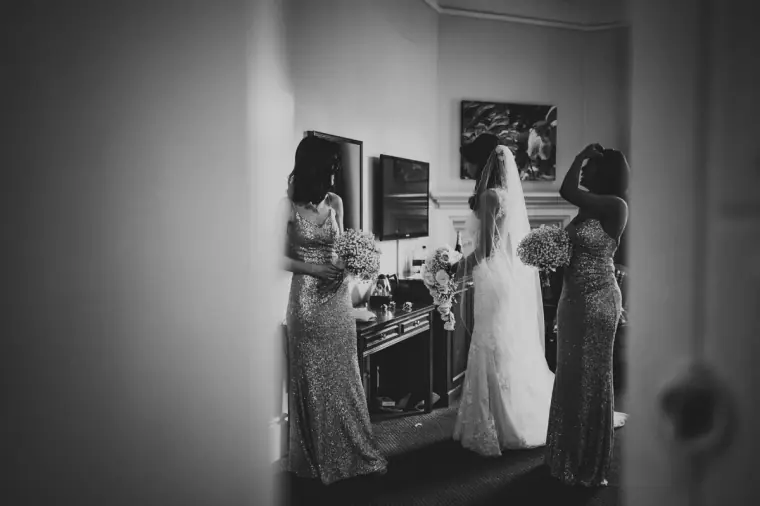 Black-and-white photo of bridesmaids helping Elina into her gown at Wotton House