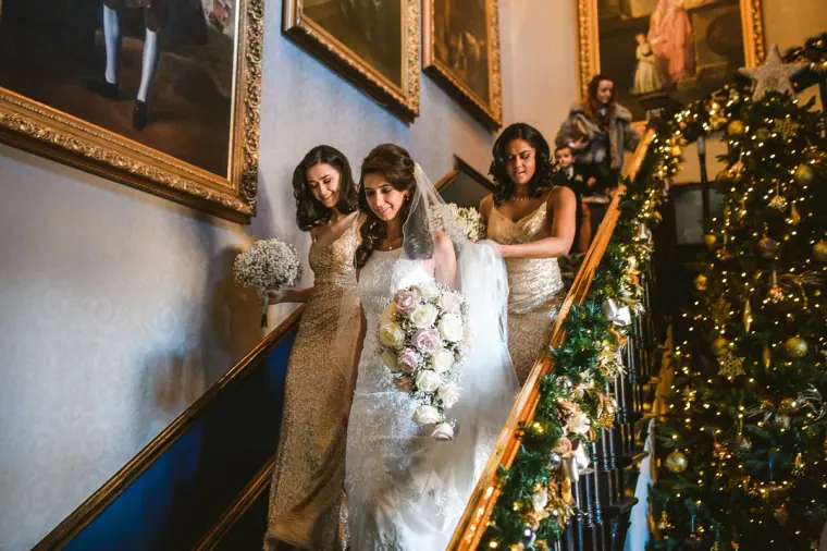 Bride and bridesmaids walking down a staircase dressed with a lit Christmas garland