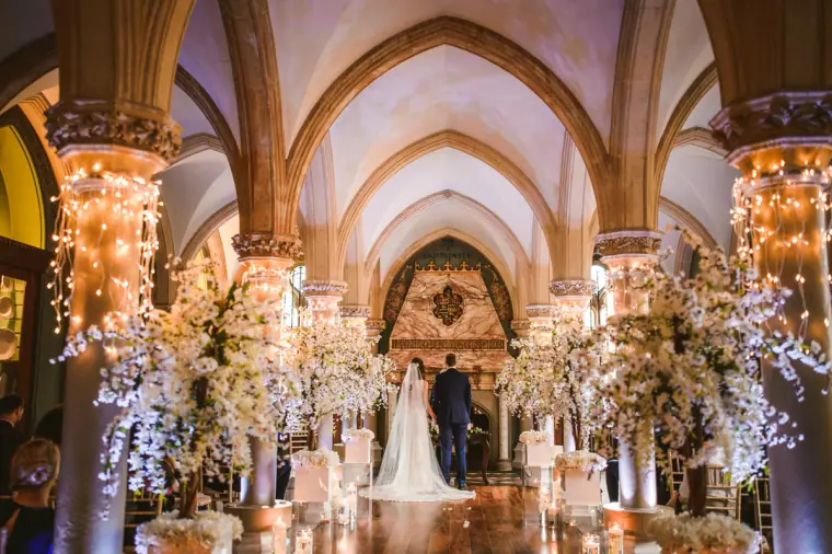 Wide view of the vaulted, blossom-filled ceremony room as the bride reaches the altar at Wotton House