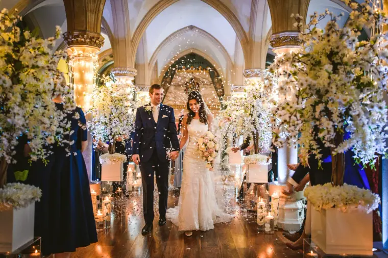 Newlyweds walking back up the aisle past guests and white blossom arrangements