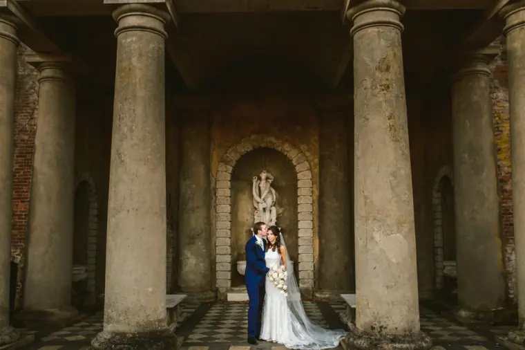Elina and Iain beneath a classical stone portico with a statue niche at Wotton House