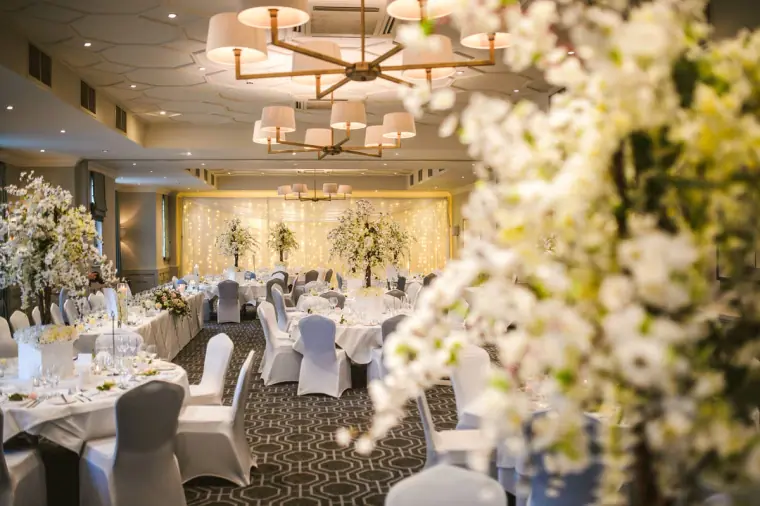 Reception room set with white-draped tables and blossom centrepieces before guests arrive