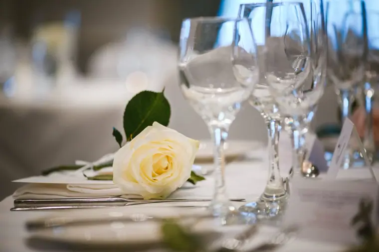 Place setting with a white rose, folded napkin and crystal glasses