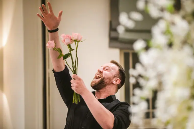Singing waiter flourishing a pink rose with arms raised during the wedding breakfast