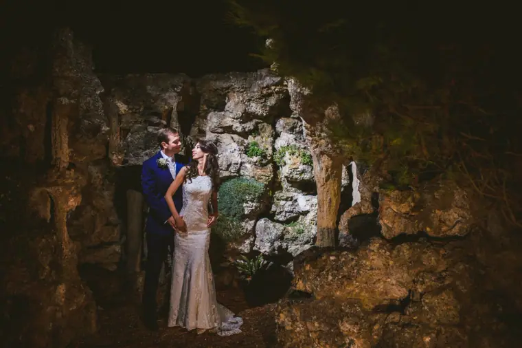Couple standing in a dramatically lit rocky grotto at night at Wotton House
