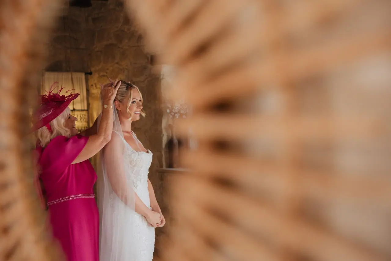 Zoe and her mum reflected in a rattan mirror as the veil is pinned