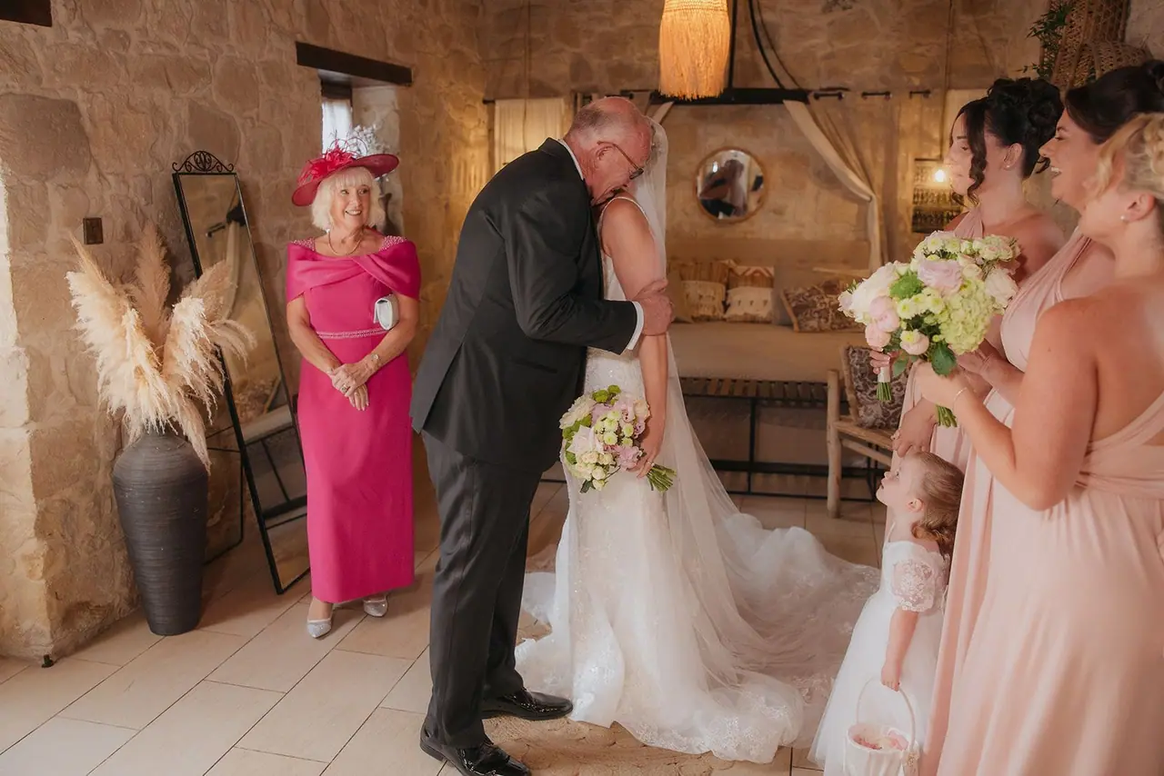 Zoe's dad kissing her as her mum and bridesmaids look on