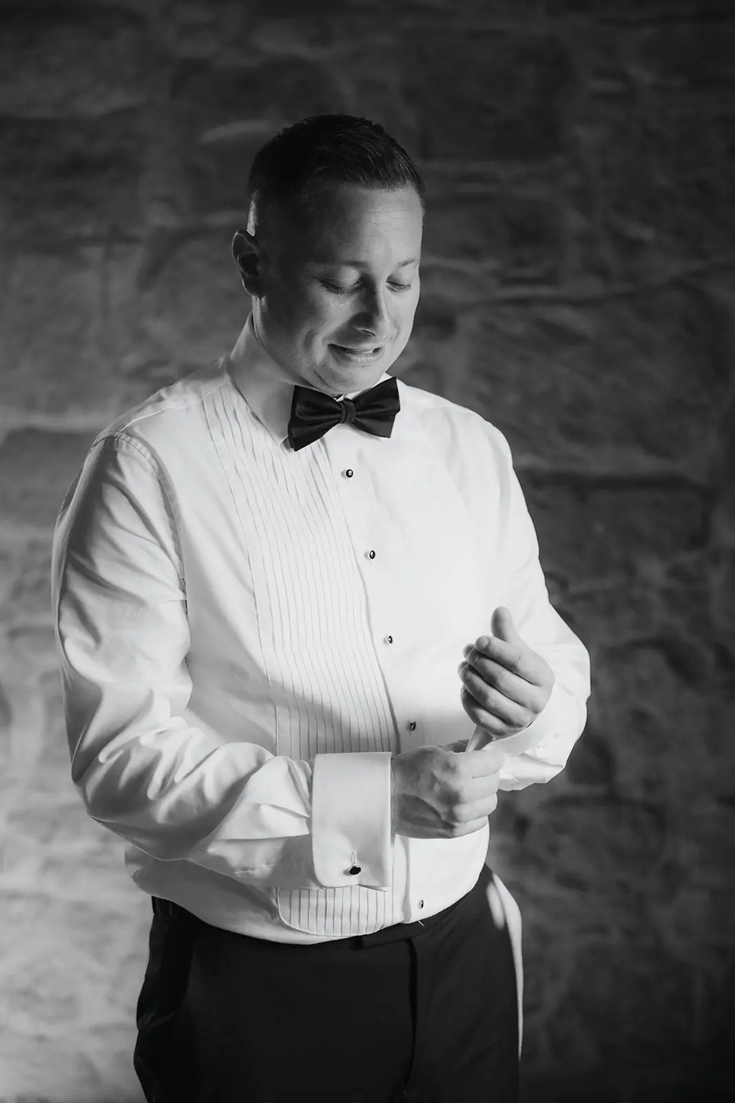 Black-and-white photo of Oliver fastening his cufflinks against a stone wall
