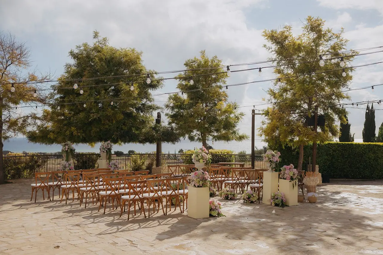 Wide view of the Liopetro ceremony terrace under string lights with trees and sea beyond