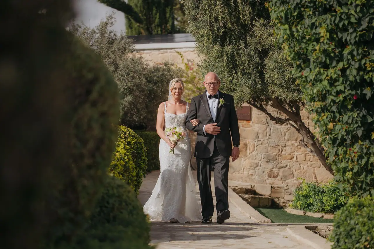 Zoe walking towards the ceremony terrace on her dad's arm between the hedges