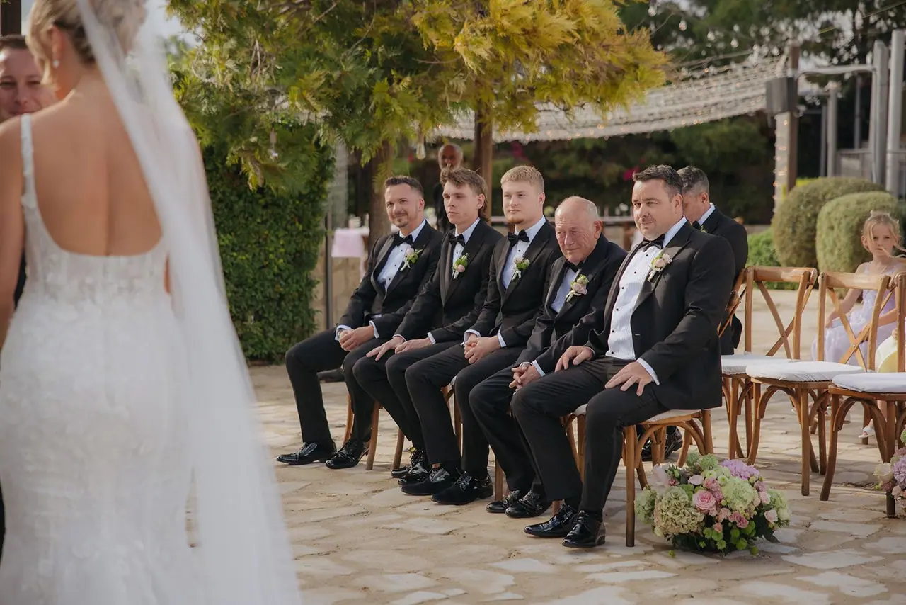 The groomsmen watching from the front row as Zoe reaches the arch