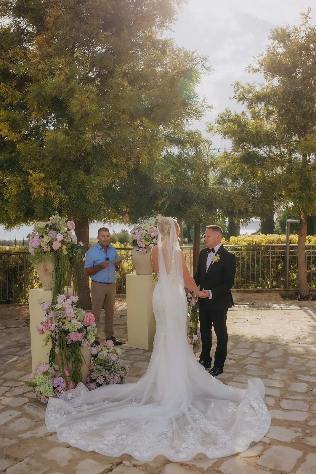 Zoe and Oliver holding hands during their vows, her train spread across the stone