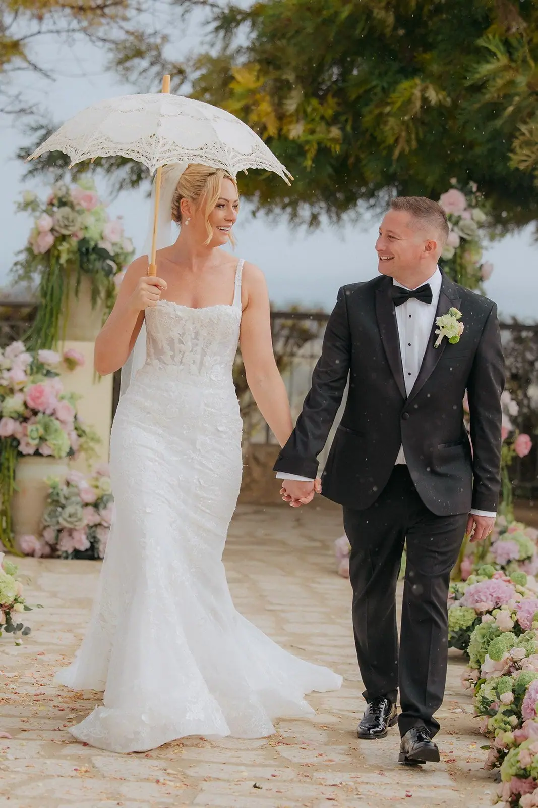 Zoe and Oliver walking hand in hand under a lace parasol