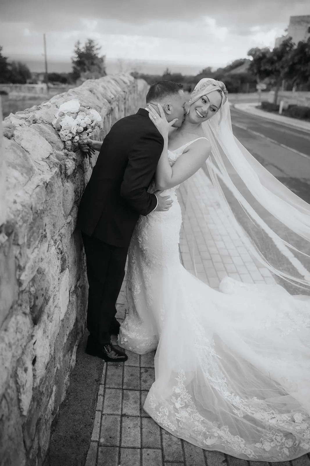 Black-and-white photo of Zoe and Oliver laughing against the stone wall