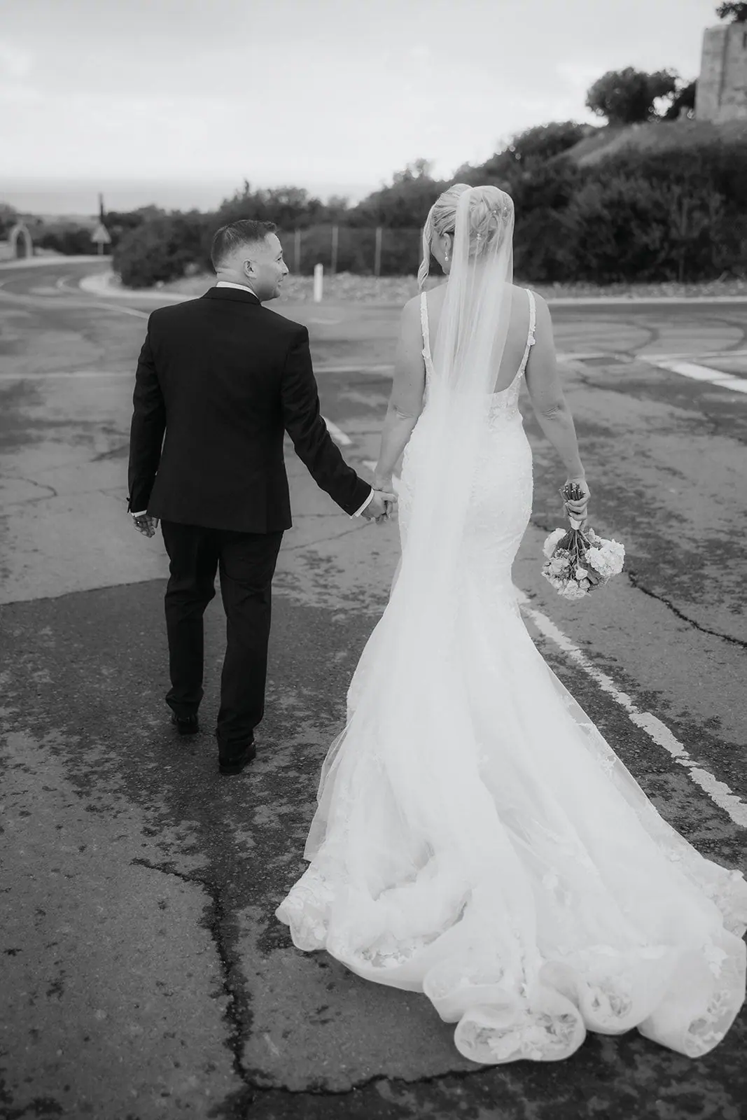 Black-and-white photo of Zoe and Oliver walking down the road, her train behind her