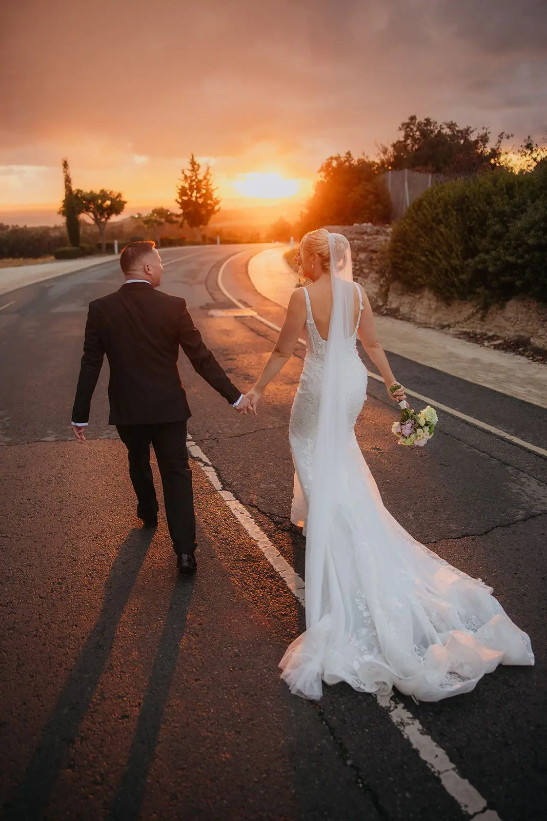 Zoe and Oliver walking hand in hand down the empty road towards the low sun