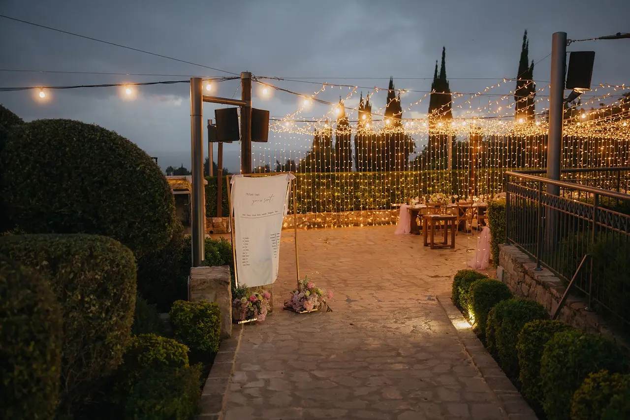 Fairy-lit path through the topiary to the reception terrace at Liopetro at dusk