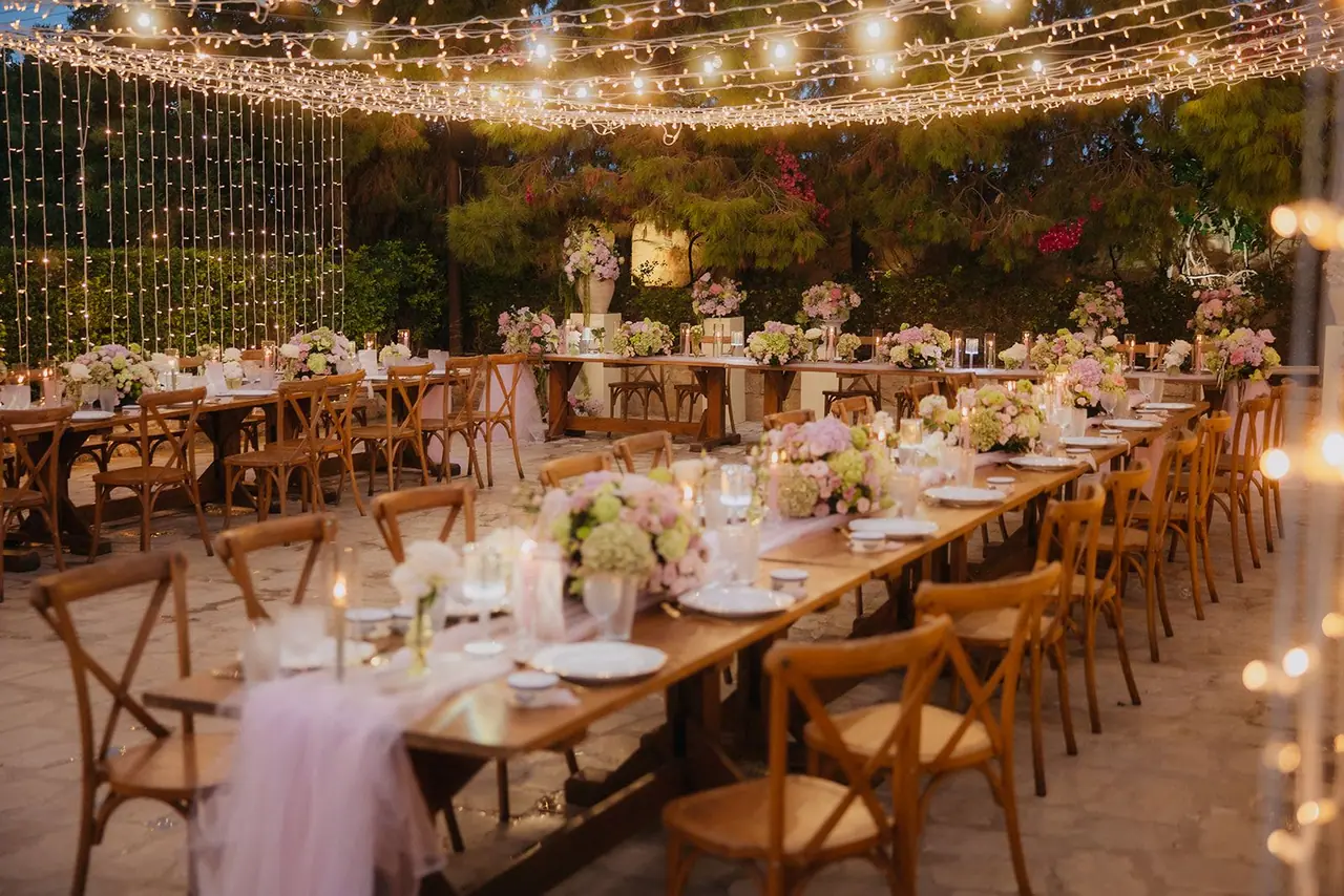 Long wooden tables dressed with flowers and candles under fairy lights at Liopetro