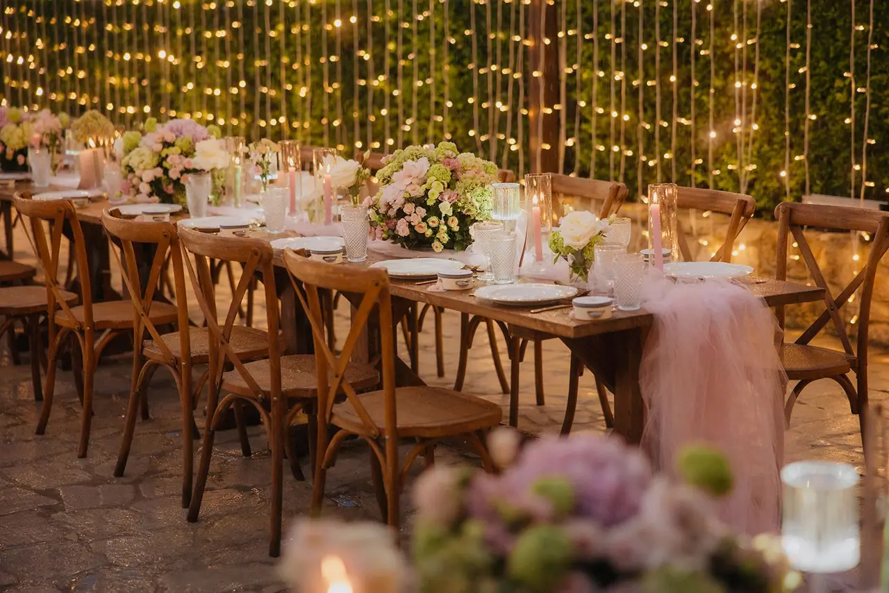 Wooden cross-back chairs along a candlelit reception table
