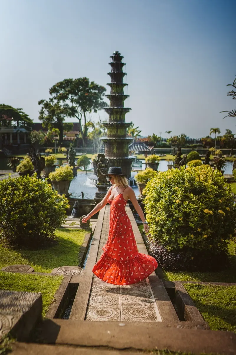 Woman in a flowing red dress walking a garden path towards a tiered pagoda in Bali