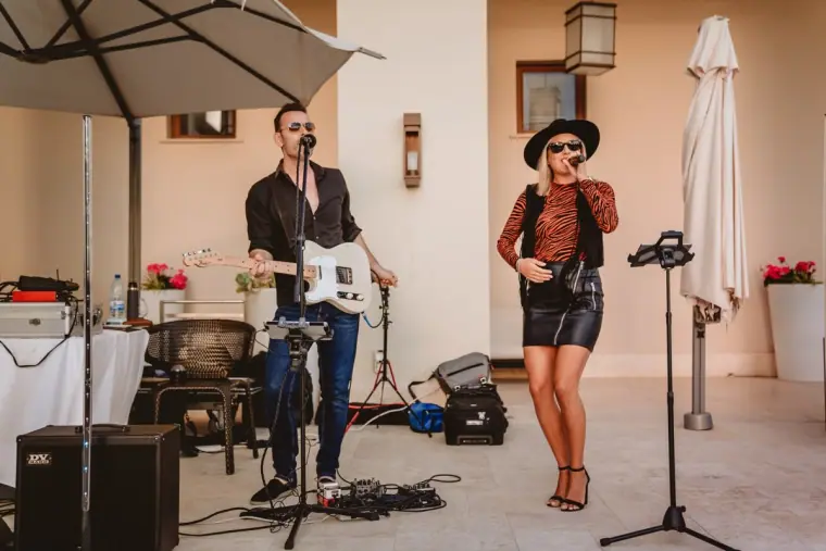 Aimie Wild and a guitarist performing live on a villa terrace beside parasols