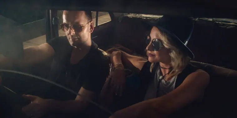 Aimie Wild and a bandmate in sunglasses in a vintage car, wide crop