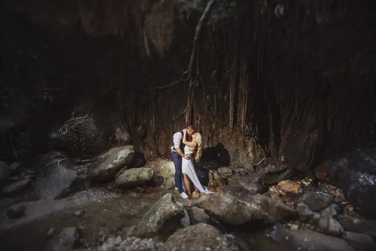 Couple kissing on boulders in a dark, tree-lined gorge