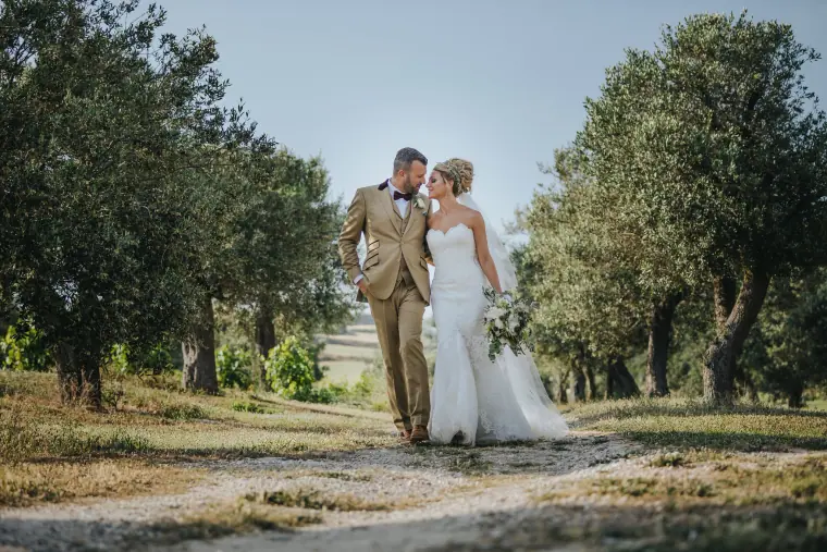 Nick and Aimie Wild walking hand in hand between olive trees on their own wedding day in Cyprus