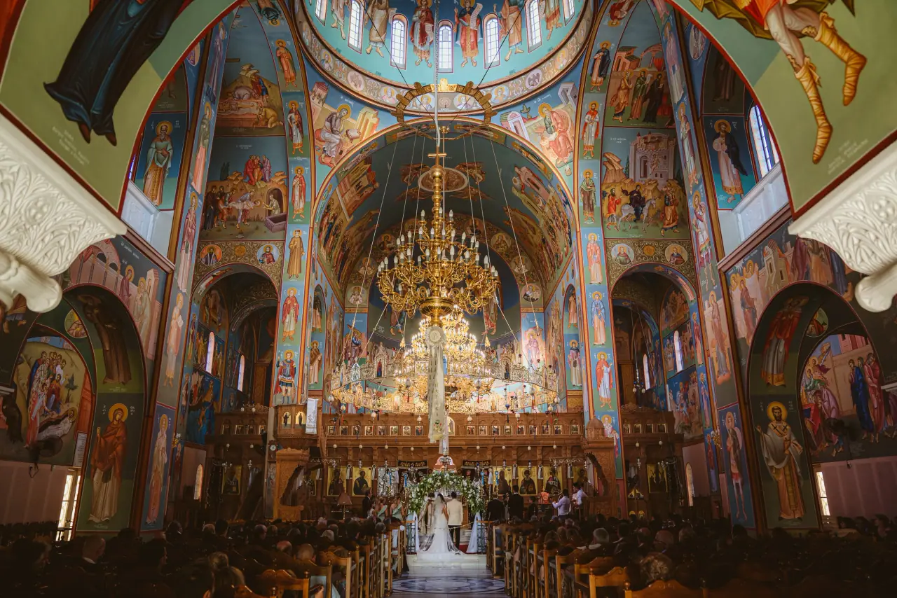 Ornately frescoed Orthodox church interior with gilded chandeliers at Andy and Stephanie's wedding